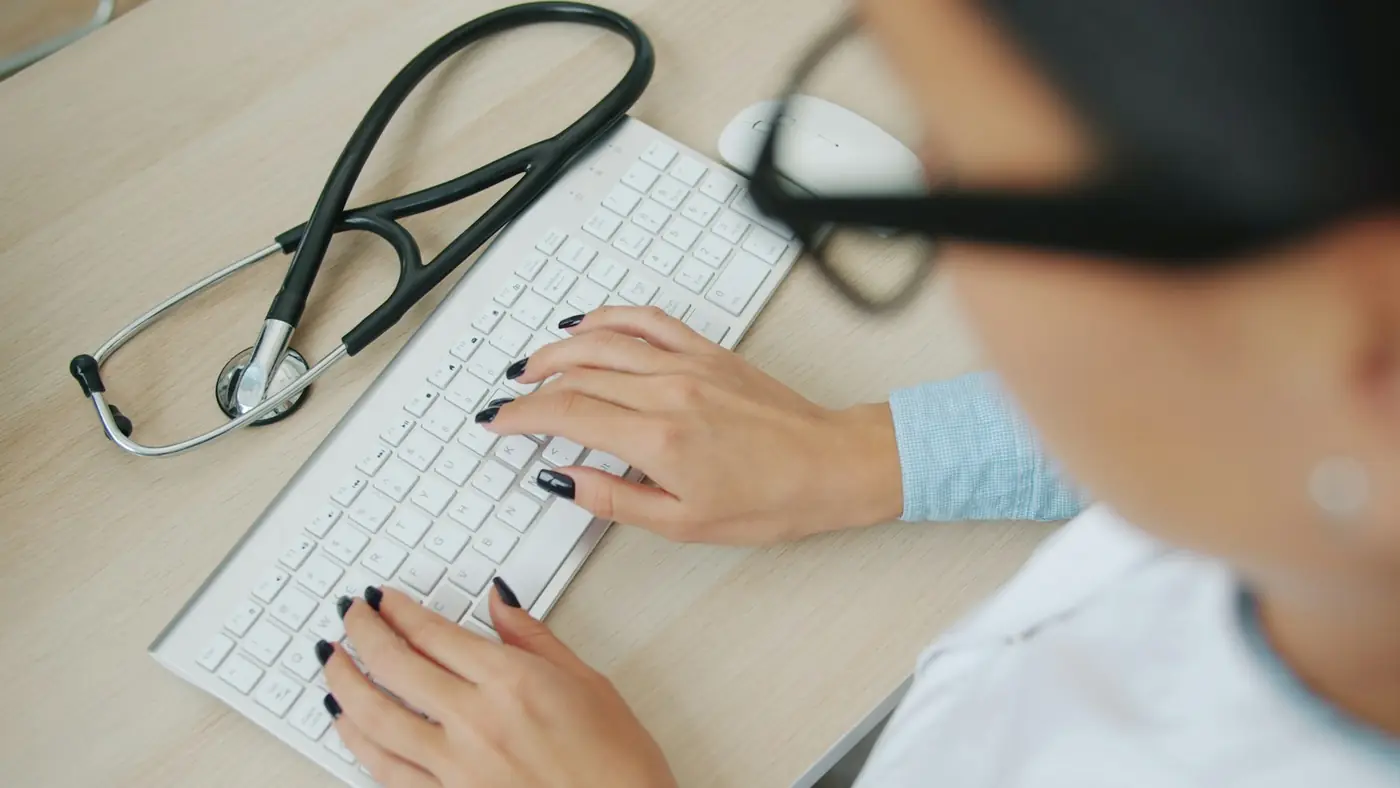 A clinician typing notes on a keyboard next to a stethoscope